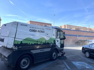 Camión de limpieza de la ciudad con el lema "Cuida Alcalá" en una calle de Alcalá de Henares, estacionado junto a varios coch