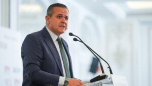 Hombre de pie frente a un podio con micrófono, hablando en un evento formal en Alcalá de Henares.