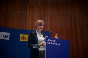 Una mujer habla en un atril con un cartel que dice "Abortar sin barreras", en un ambiente de conferencia.