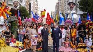 Personas vestidas con trajes coloridos, banderas de distintos países y figuras gigantes en una calle de Madrid.
