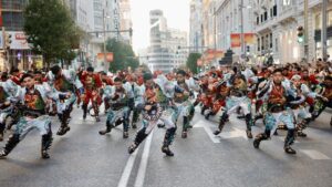 Grupo de bailarines en trajes coloridos realizando una coreografía en una calle de Madrid durante un desfile.