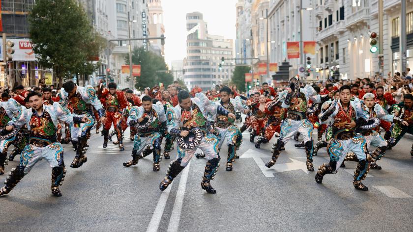Grupo de bailarines en trajes coloridos realizando una coreografía en una calle de Madrid durante un desfile.