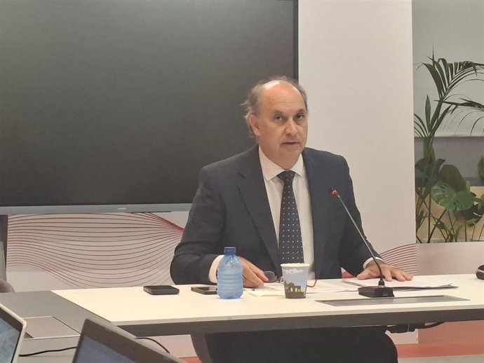 Un hombre sentado en una mesa con un micrófono, en una sala de reuniones con pantalla y plantas, en Madrid.