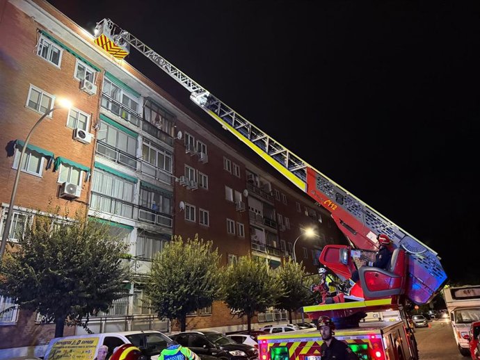Bomberos en una camioneta con escalera extensible frente a un edificio en Madrid, trabajando en la noche tras las tormentas.