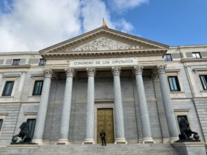 Fachada del Congreso de los Diputados con columnas y puerta dorada, flanqueada por estatuas de leones. Un guardia se encuentr