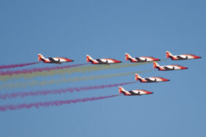 Un grupo de aviones en formación vuela en el cielo, dejando estelas de humo de diferentes colores. La imagen capta la acrobac