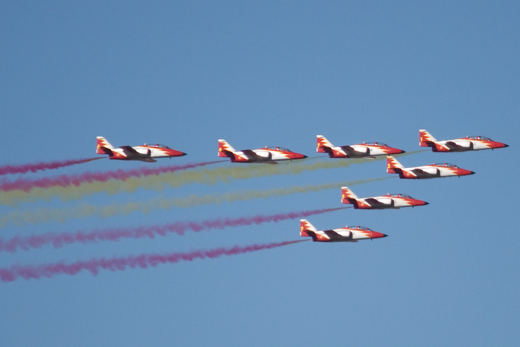 Un grupo de aviones en formación vuela en el cielo, dejando estelas de humo de diferentes colores. La imagen capta la acrobac