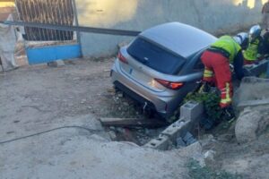 Un coche plateado accidentado en un terreno con maleza, donde varios rescatistas trabajan para auxiliar a los ocupantes.